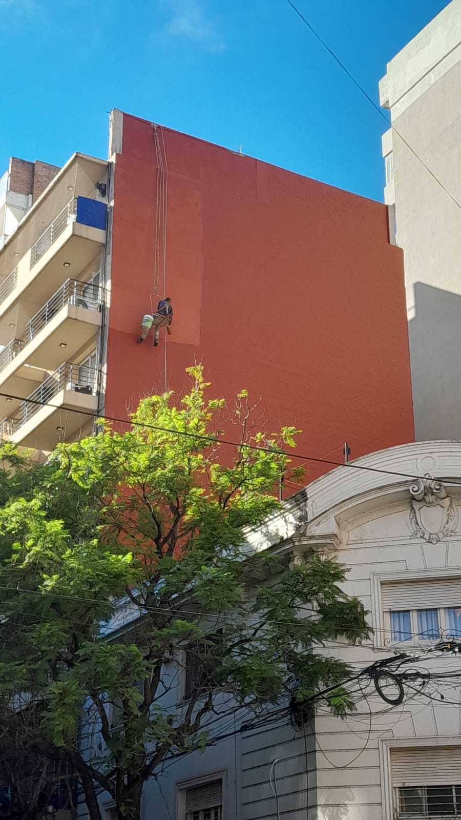 Trabajador suspendido en silleta pintando una medianera de gran altura