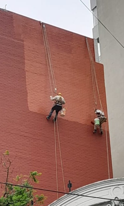 Dos trabajadores de Grupo AD suspendidos en silleta pintando una medianera