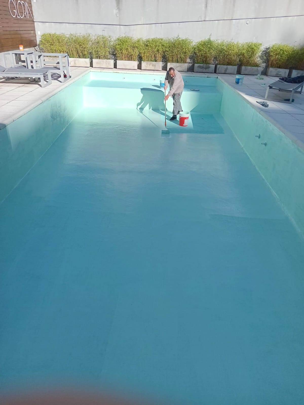 Operario aplicando pintura aguamarina en el fondo de una pileta